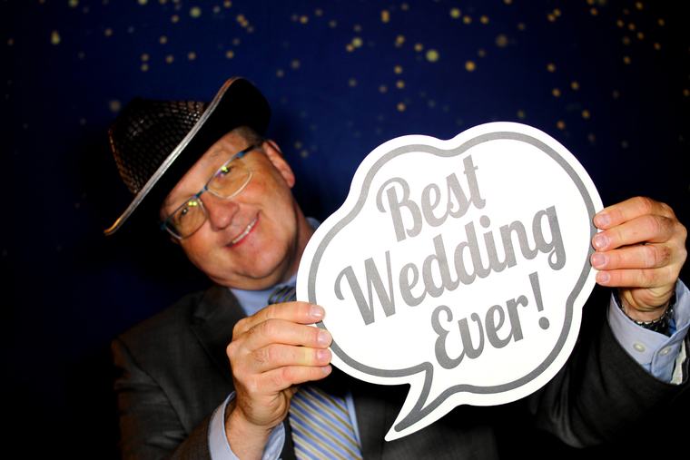 Wedding guest in a cowboy hat posing with a Best Wedding Ever photo booth prop